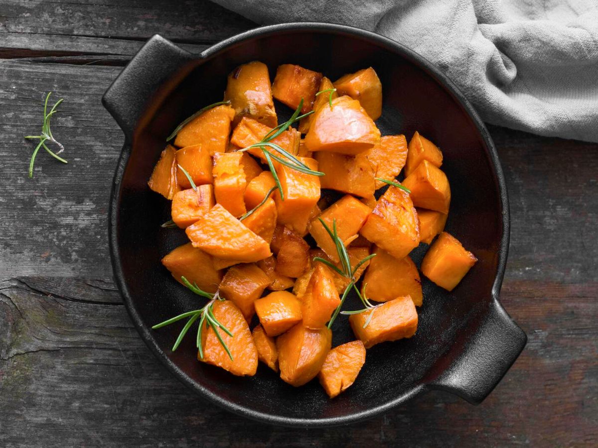 Roasted sweet potatoes garnished with rosemary in a cast iron skillet.