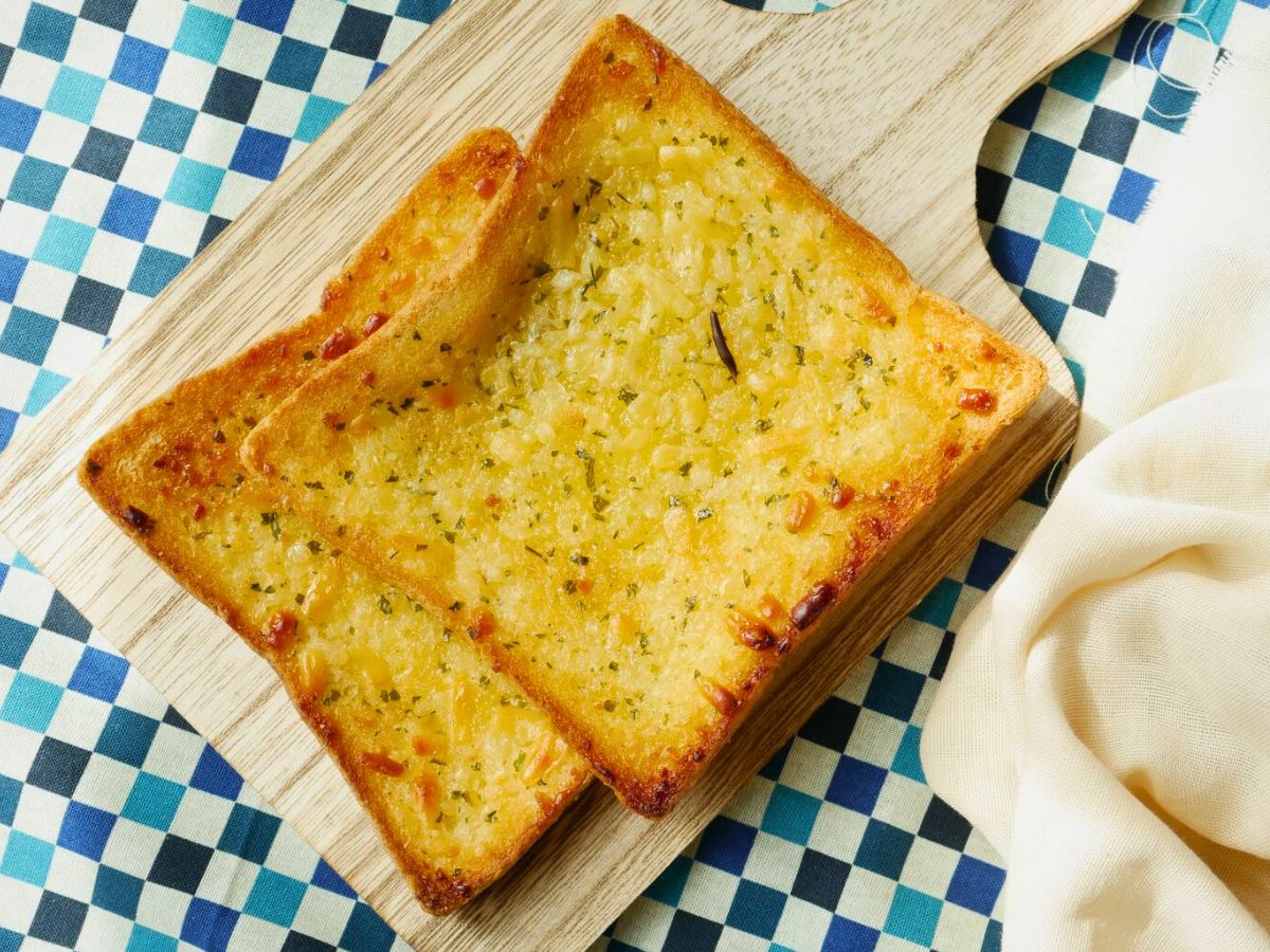 Toasted garlic bread on a wooden cutting board with a blue and white checkered tablecloth.