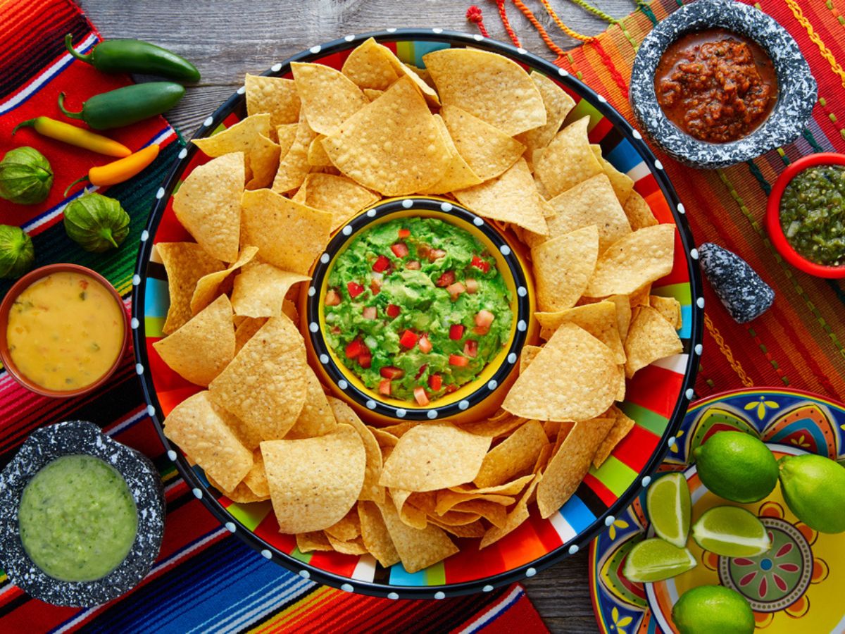 Plate of tortilla chips accompanied by various dips on a colorful tablecloth.