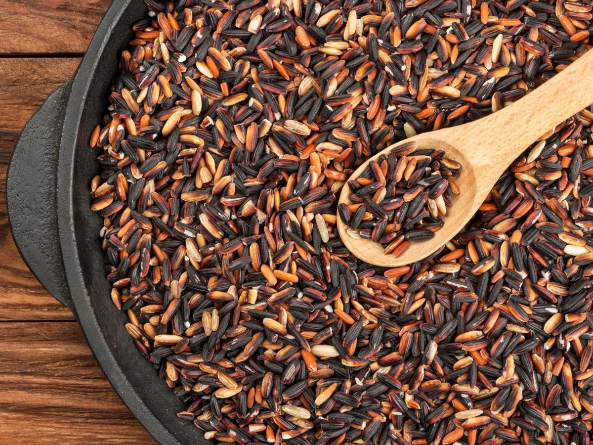 A cast iron skillet filled with wild rice and a wooden spoon on a wooden table.