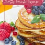 Pancakes with honey, strawberries, blueberries, and raspberries on a white plate with the text "slay the day - healthy pancake toppings.